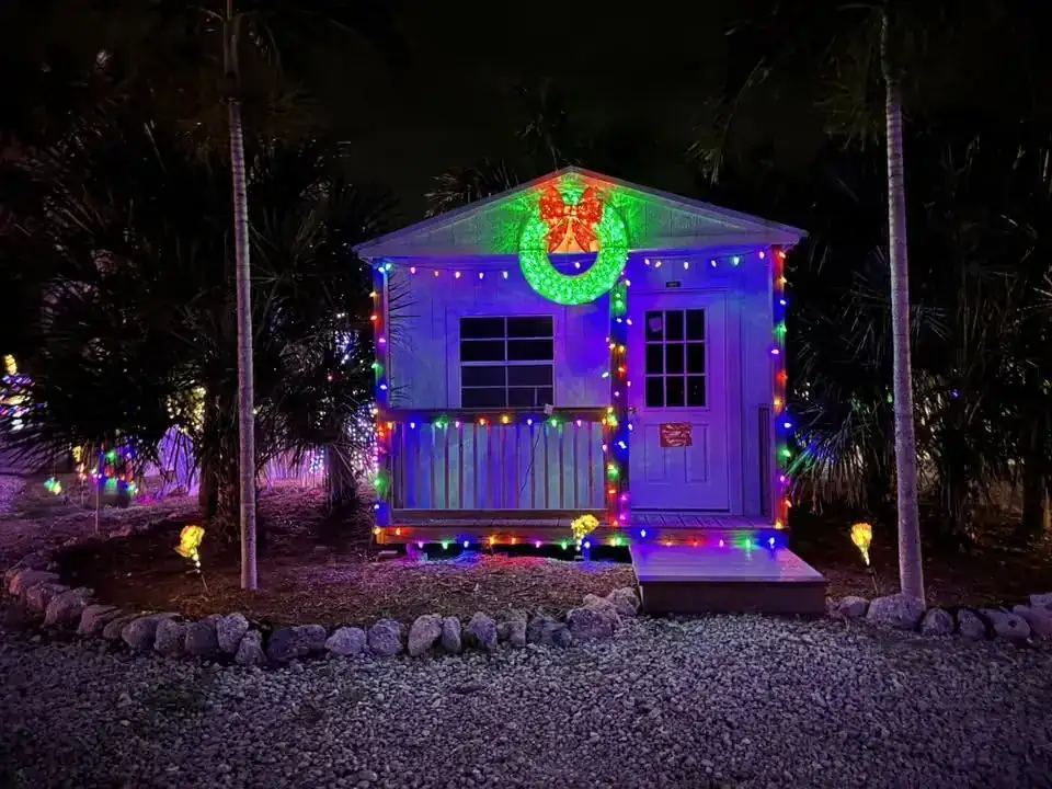 A small cabin outlined in colored lights with a wreath